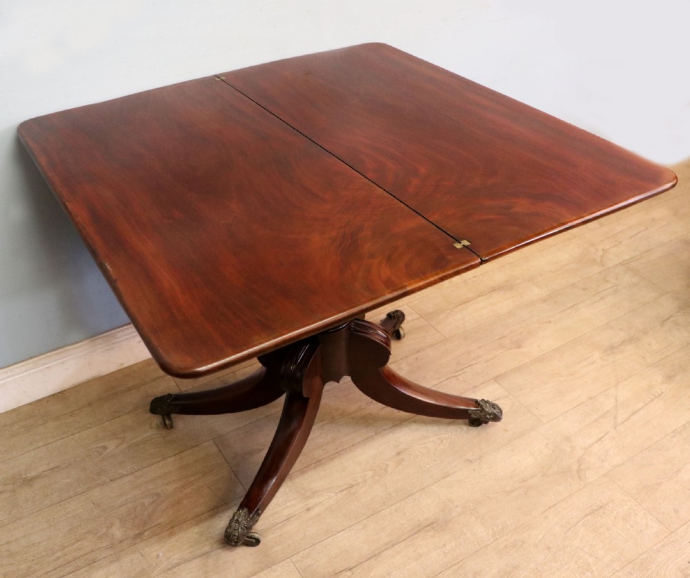An early 19th-century mahogany tea table featuring a hinged fold-over top, turned central column, and four splayed legs with brass castors. View III