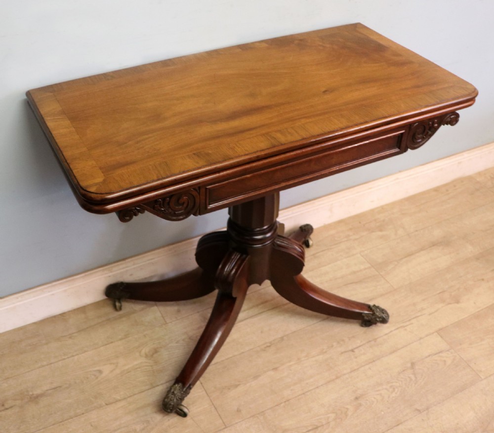 An early 19th-century mahogany tea table featuring a hinged fold-over top, turned central column, and four splayed legs with brass castors. View V