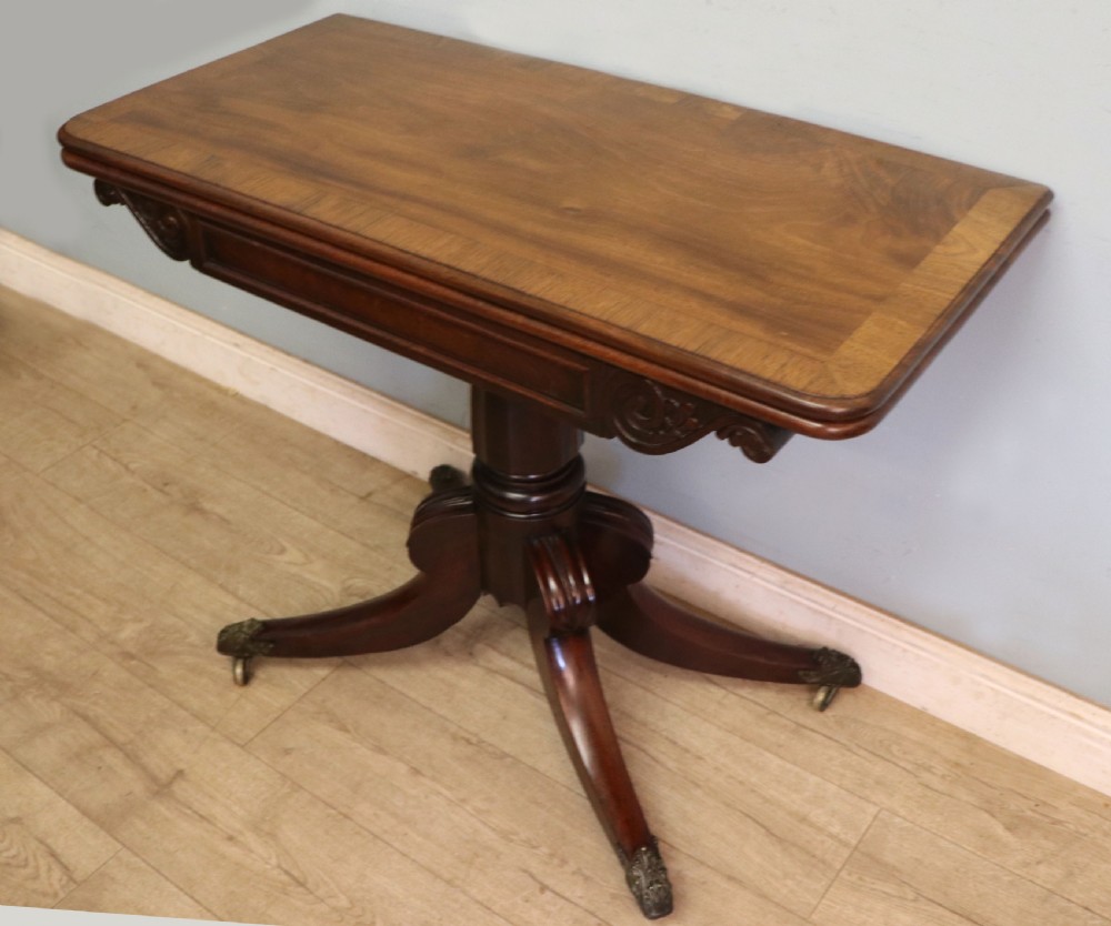 An early 19th-century mahogany tea table featuring a hinged fold-over top, turned central column, and four splayed legs with brass castors. View VI