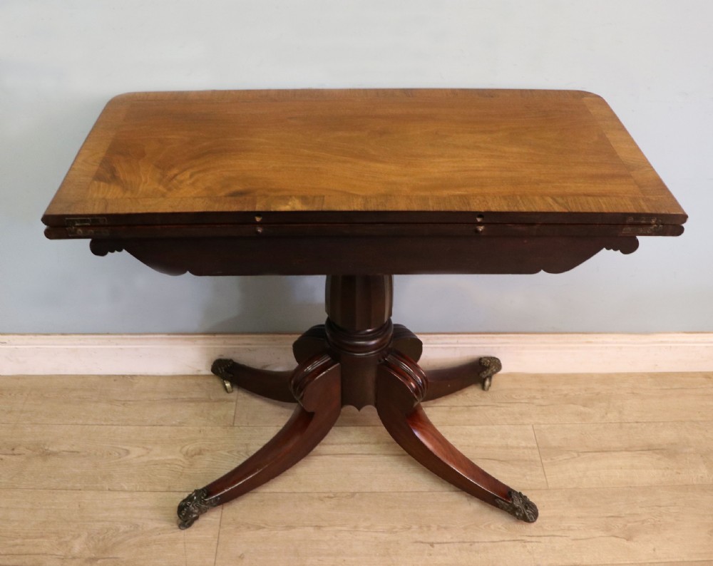 An early 19th-century mahogany tea table featuring a hinged fold-over top, turned central column, and four splayed legs with brass castors. View VII