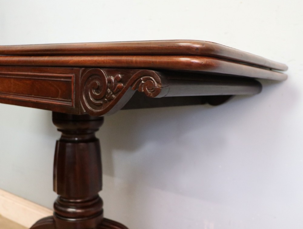 An early 19th-century mahogany tea table featuring a hinged fold-over top, turned central column, and four splayed legs with brass castors. View X