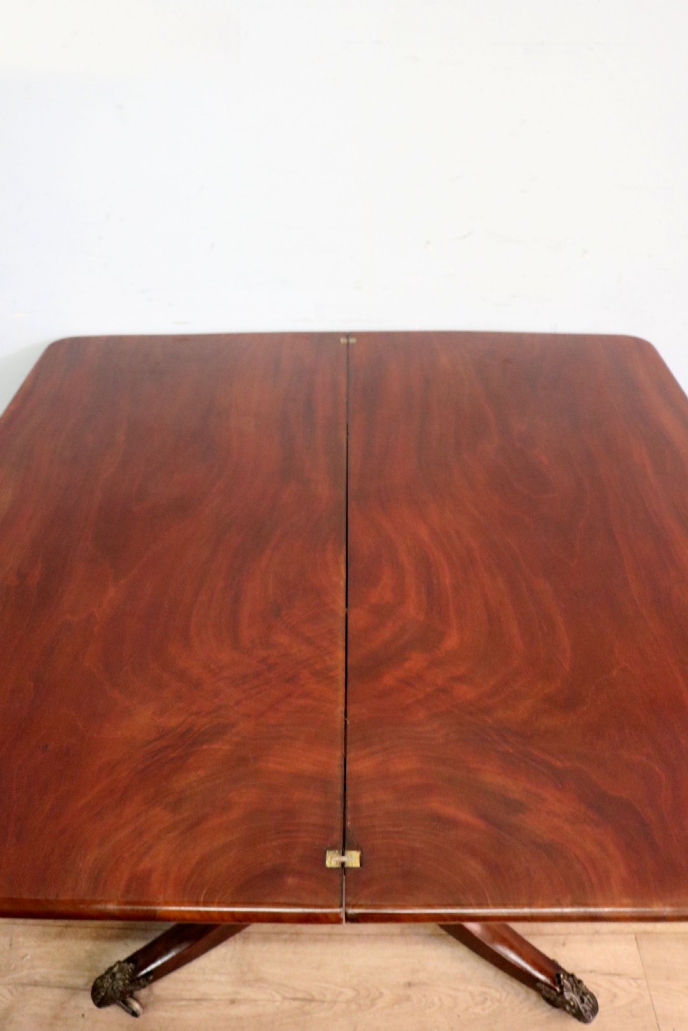An early 19th-century mahogany tea table featuring a hinged fold-over top, turned central column, and four splayed legs with brass castors. View XII