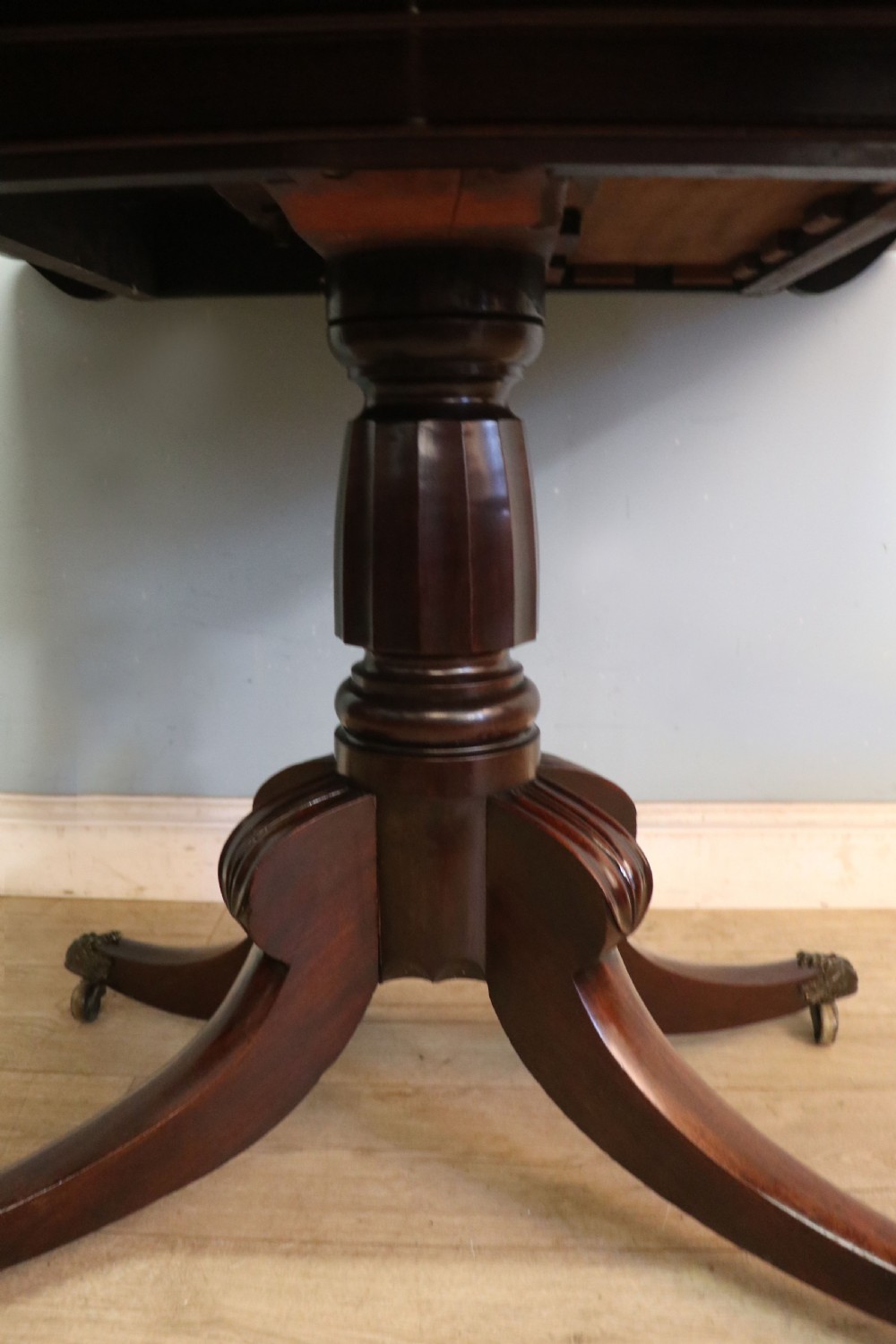 An early 19th-century mahogany tea table featuring a hinged fold-over top, turned central column, and four splayed legs with brass castors. View XX