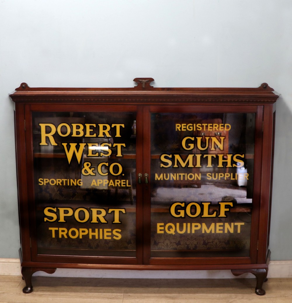 A late nineteenth-century dark mahogany display cabinet featuring two glazed doors adorned with hand-painted gold advertising typography, resting on short cabriole legs.
