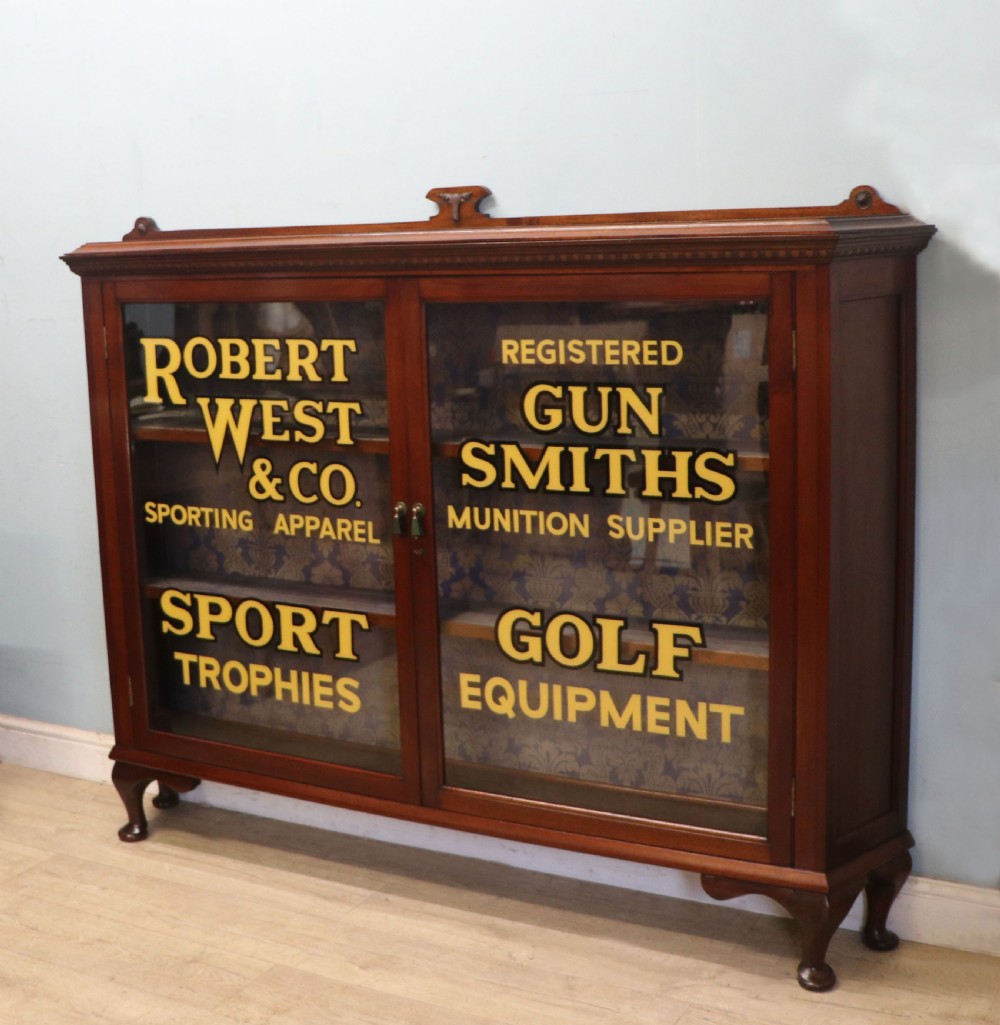 A late nineteenth-century dark mahogany display cabinet featuring two glazed doors adorned with hand-painted gold advertising typography, resting on short cabriole legs. View II
