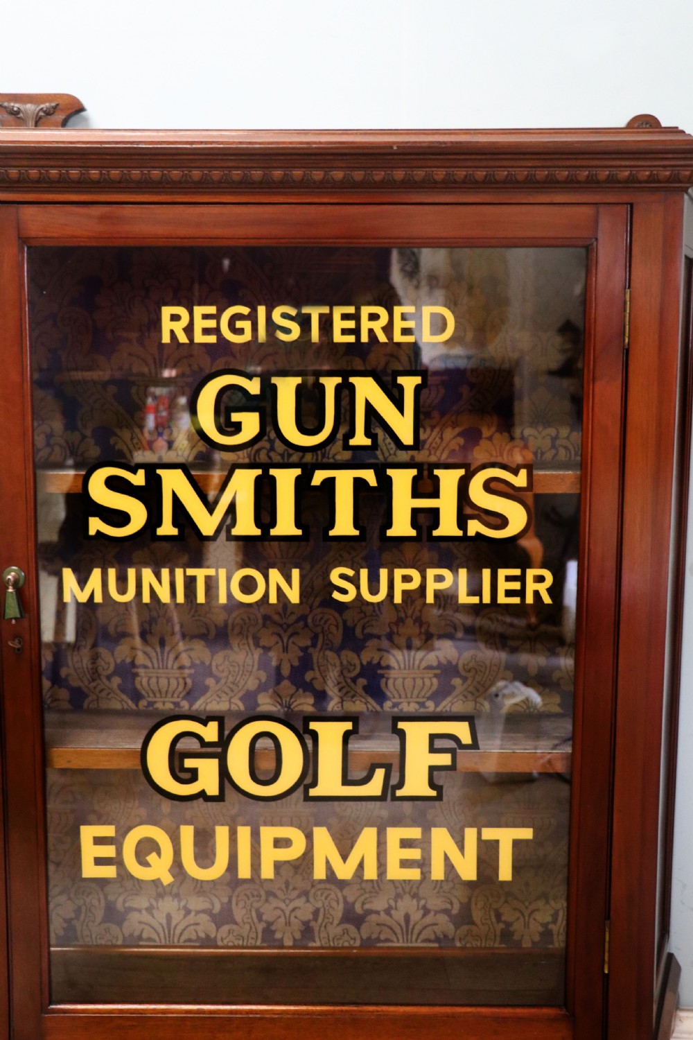 A late nineteenth-century dark mahogany display cabinet featuring two glazed doors adorned with hand-painted gold advertising typography, resting on short cabriole legs. View IV
