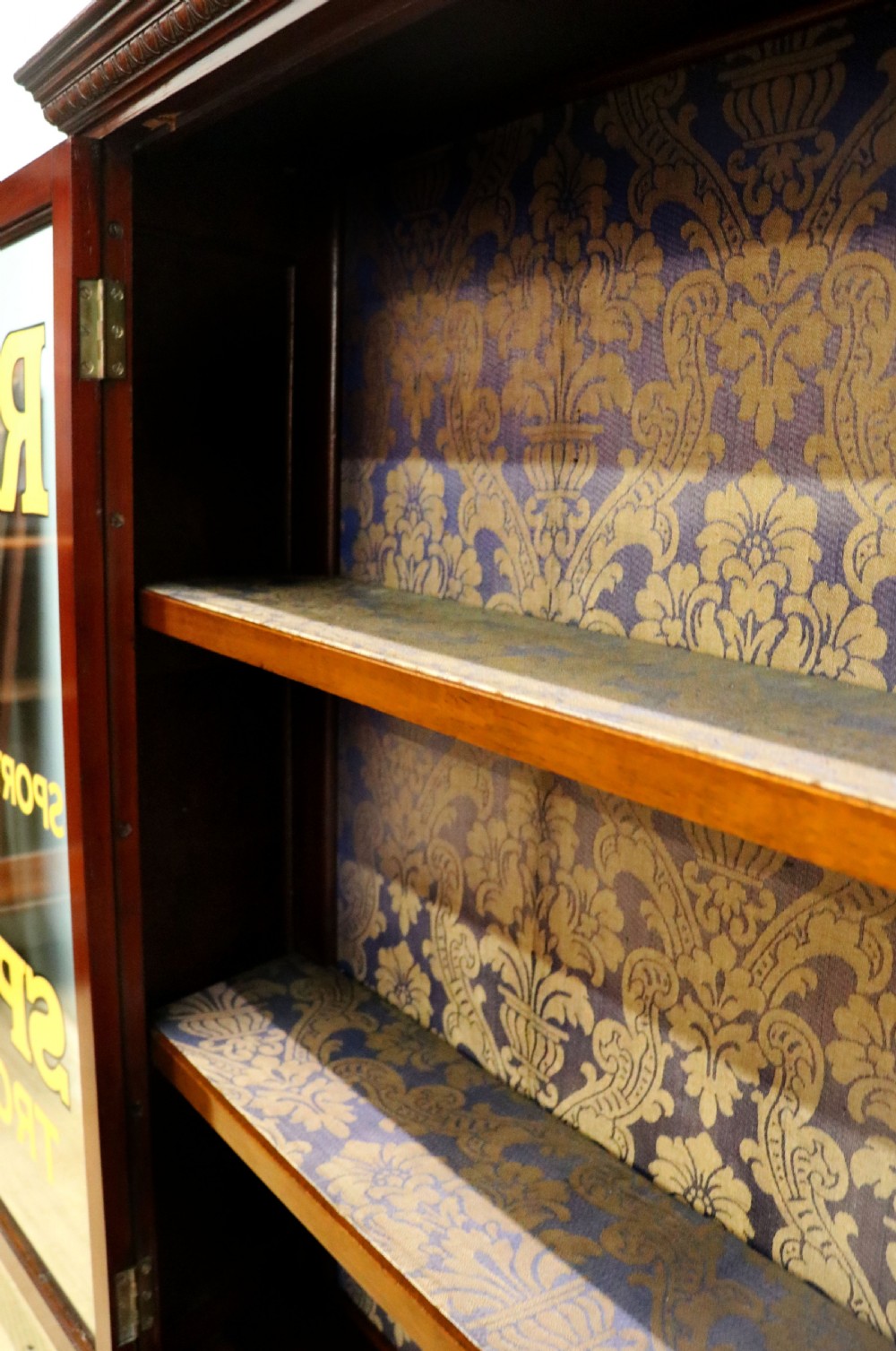 A late nineteenth-century dark mahogany display cabinet featuring two glazed doors adorned with hand-painted gold advertising typography, resting on short cabriole legs. View XXI