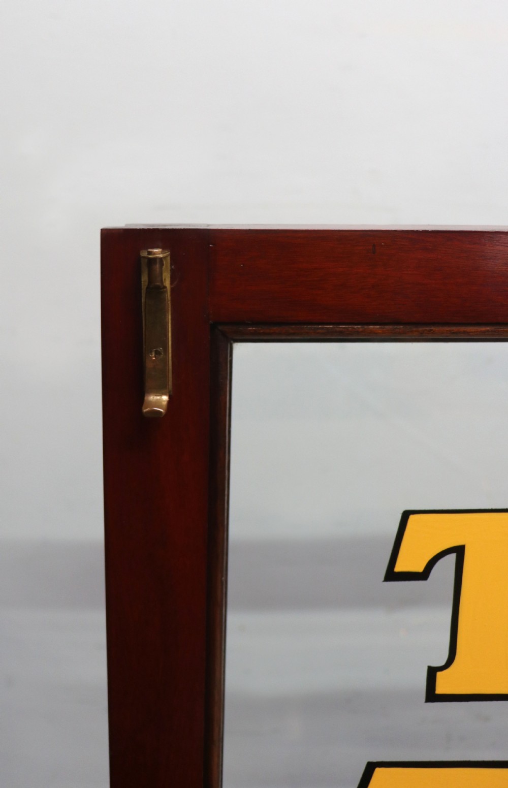 A late nineteenth-century dark mahogany display cabinet featuring two glazed doors adorned with hand-painted gold advertising typography, resting on short cabriole legs. View XXII