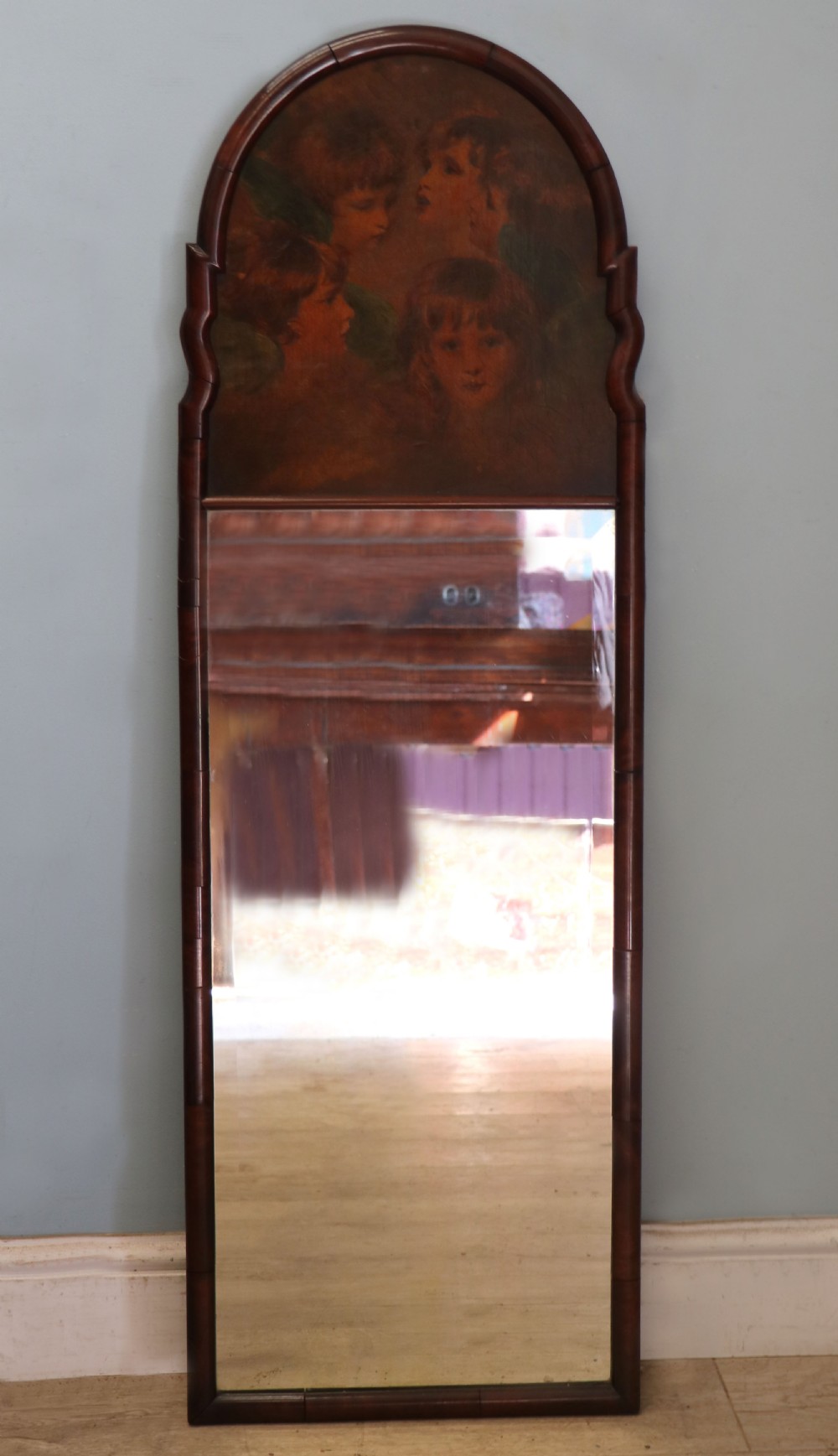 A tall, arched 19th-century mahogany wall mirror featuring an upper oil painting of childrens faces above a rectangular mirror glass.