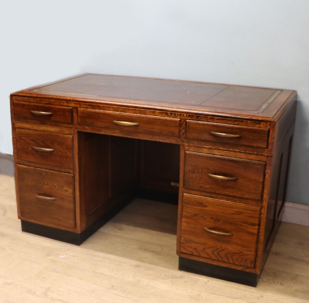 A twin-pedestal mid-century oak office desk featuring seven drawers with brass pull handles and a dark plinth base. View II