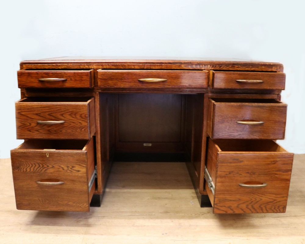 A twin-pedestal mid-century oak office desk featuring seven drawers with brass pull handles and a dark plinth base. View III