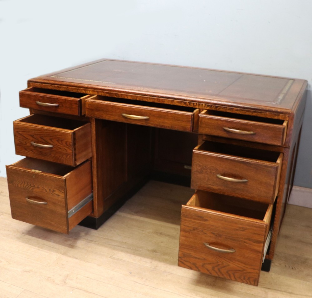 A twin-pedestal mid-century oak office desk featuring seven drawers with brass pull handles and a dark plinth base. View IV