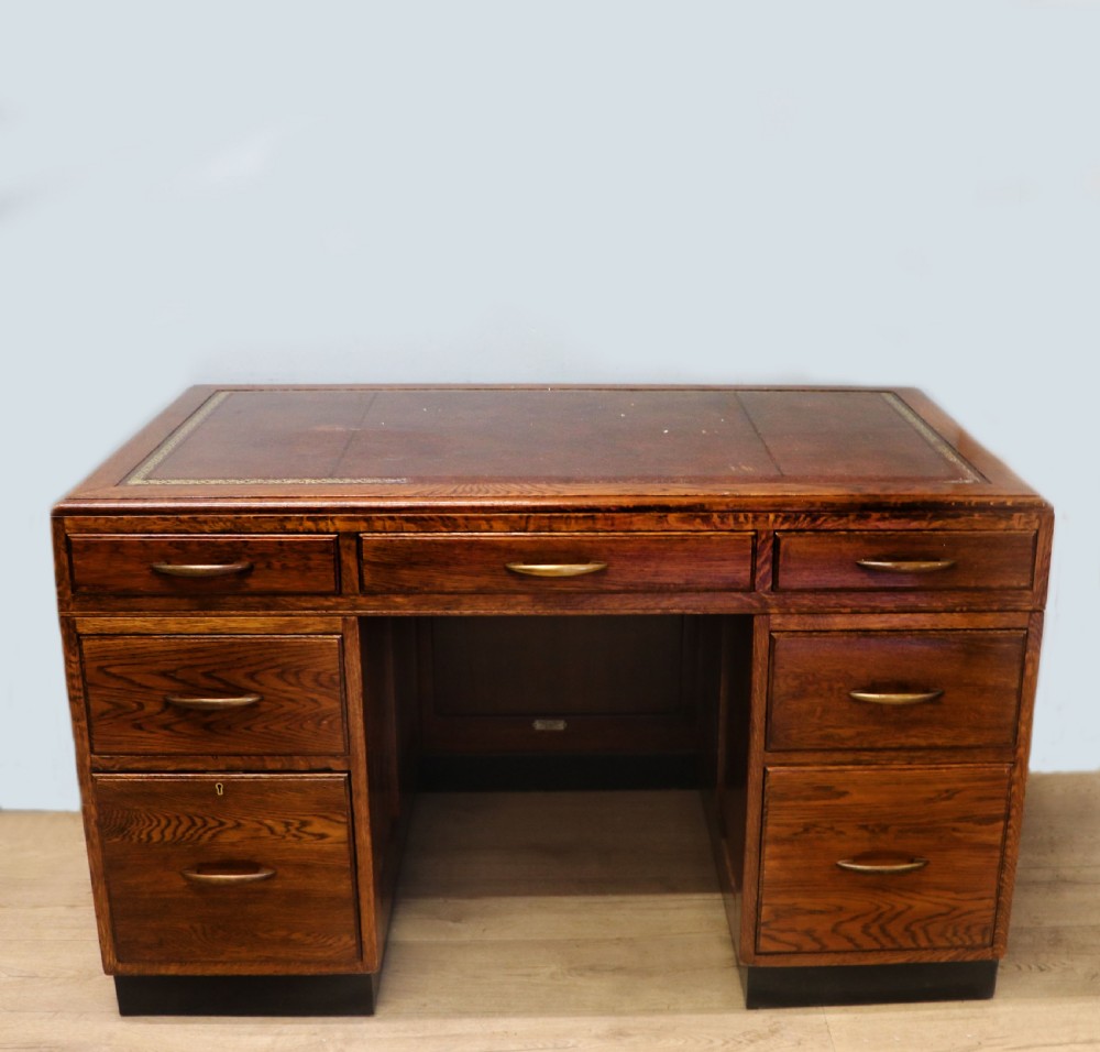 A twin-pedestal mid-century oak office desk featuring seven drawers with brass pull handles and a dark plinth base. View VII