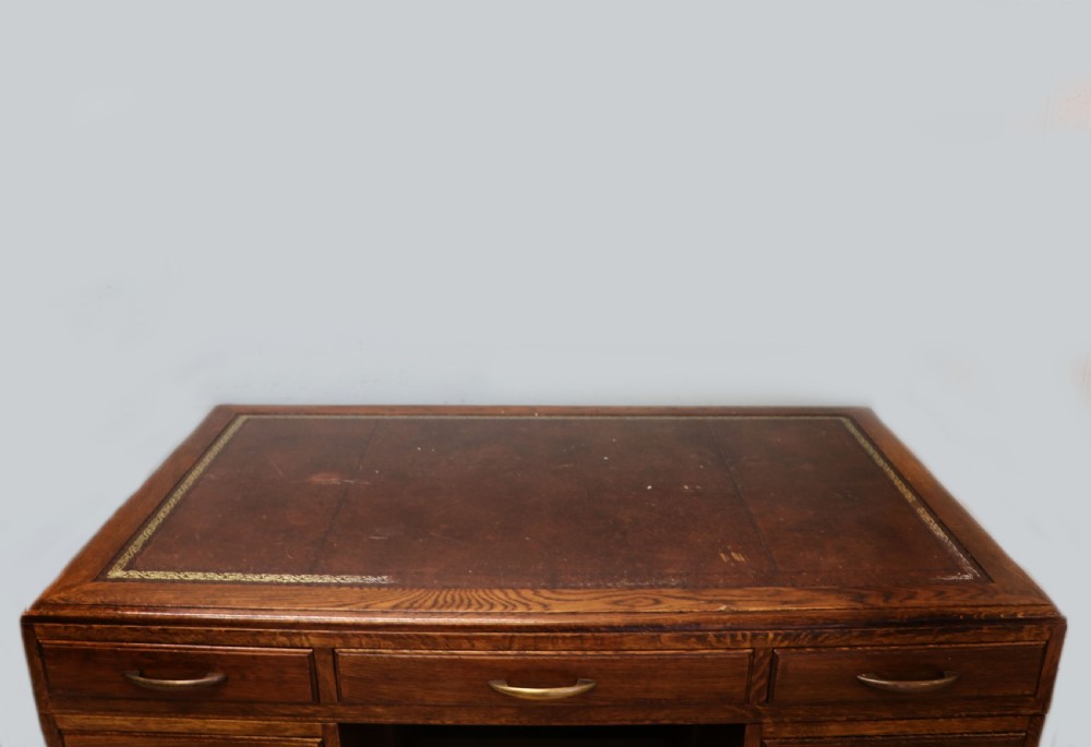 A twin-pedestal mid-century oak office desk featuring seven drawers with brass pull handles and a dark plinth base. View VIII
