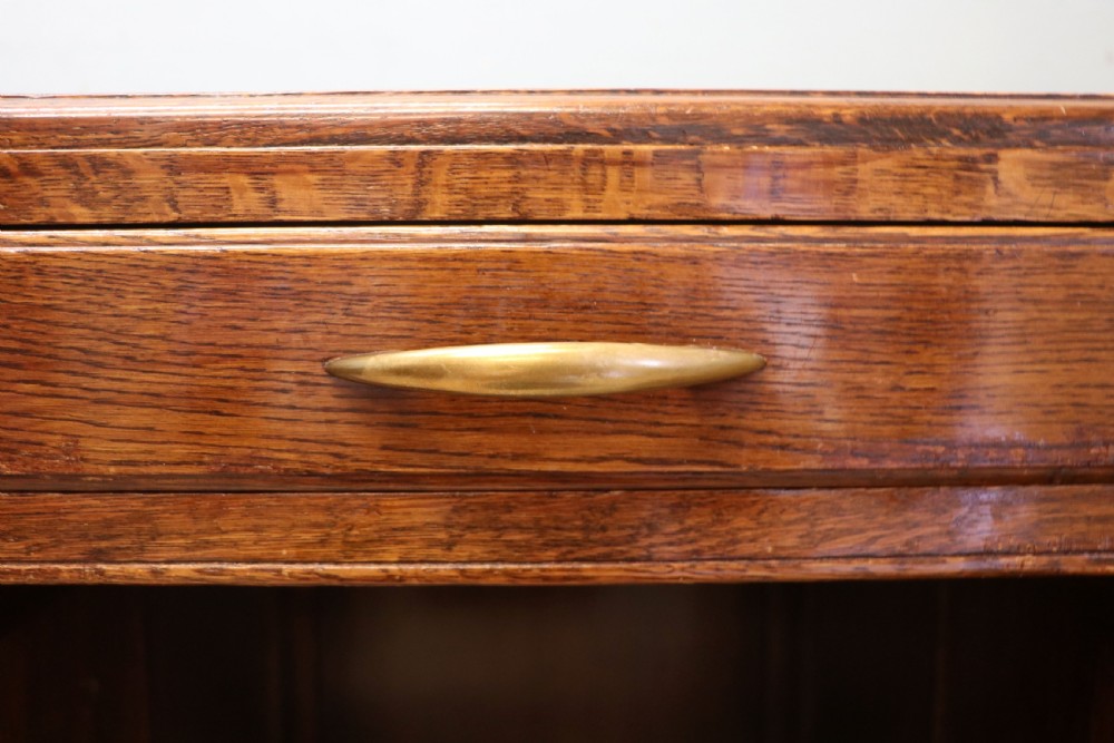 A twin-pedestal mid-century oak office desk featuring seven drawers with brass pull handles and a dark plinth base. View X