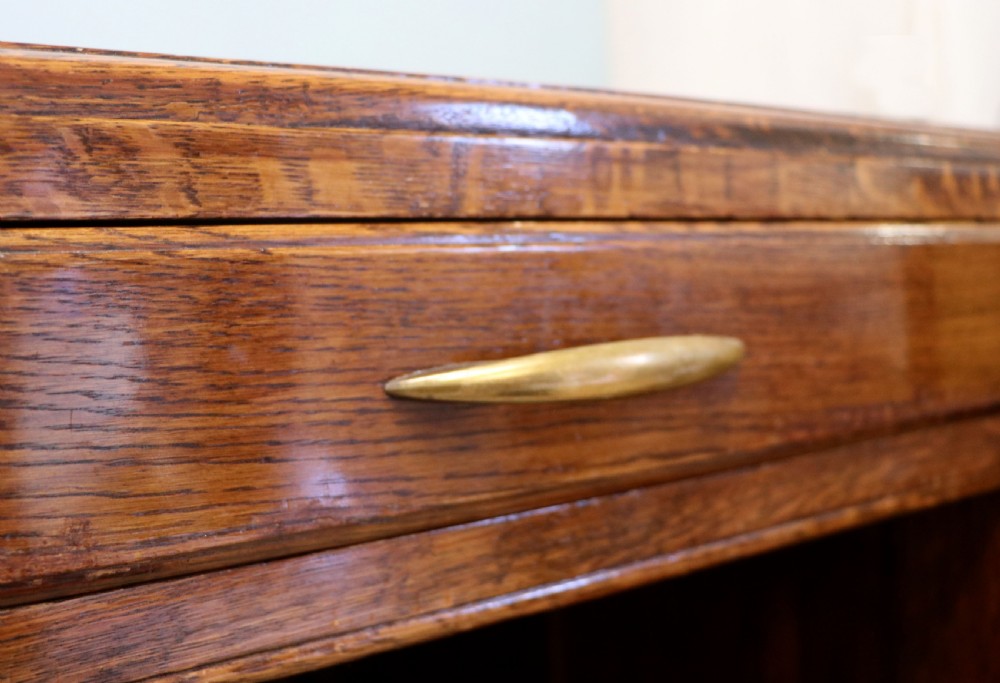 A twin-pedestal mid-century oak office desk featuring seven drawers with brass pull handles and a dark plinth base. View XI