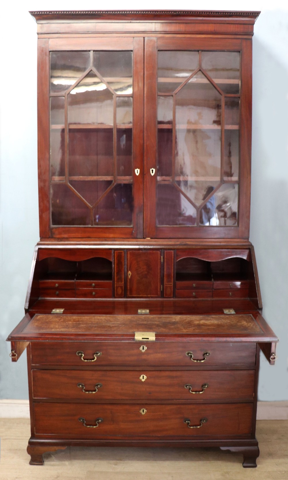 Late eighteenth-century mahogany bureau bookcase with an upper glazed cabinet featuring geometric astragal bars, an open fall-front writing surface, and lower drawers with brass handles.