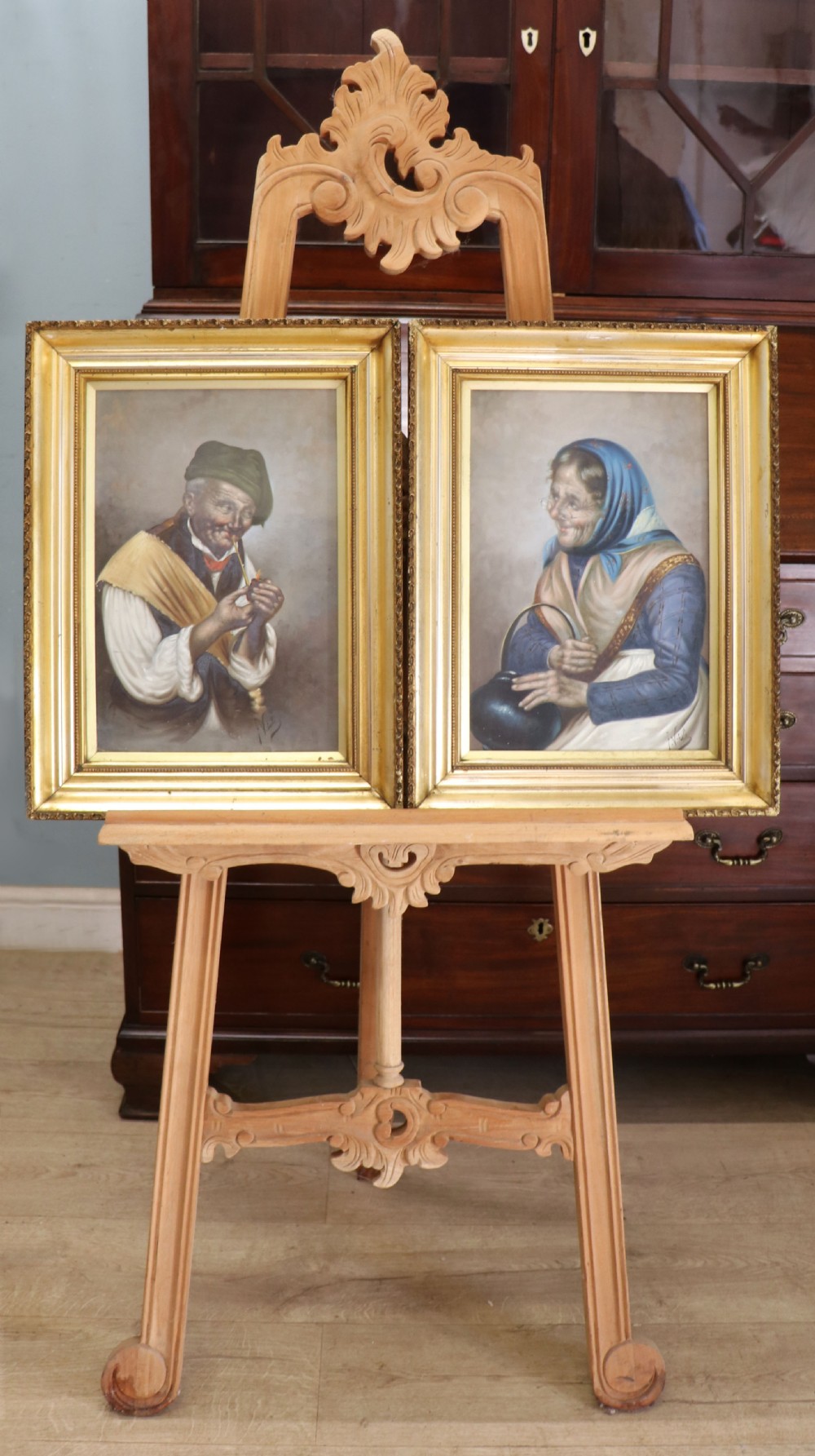 A pair of framed Italian oil portraits depicting an elderly man smoking a pipe and an elderly woman wearing a blue headscarf, both set in matching giltwood frames.