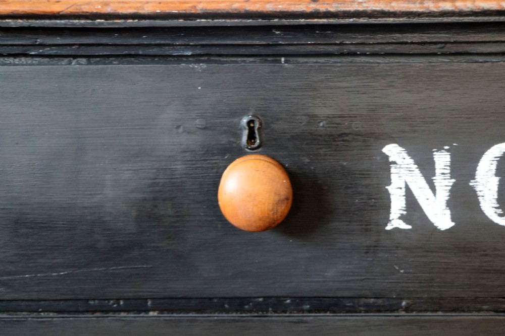 A Victorian black painted pine chest of drawers featuring a natural timber top with hand-painted lettering and turned wooden knobs. View XIII