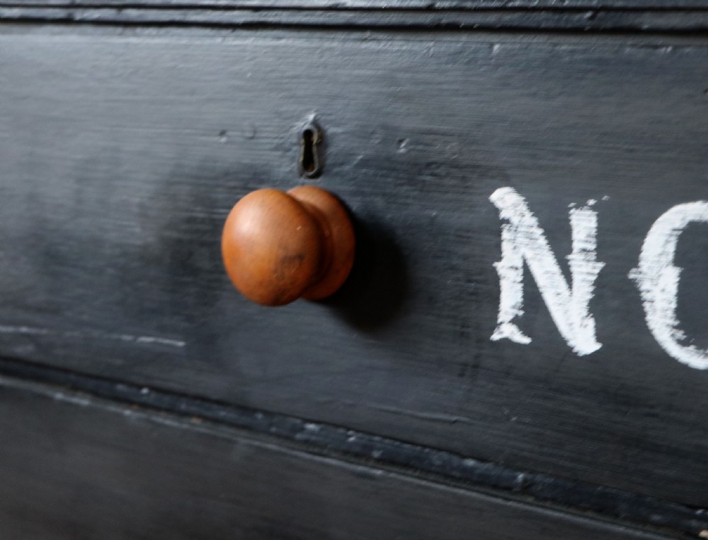 A Victorian black painted pine chest of drawers featuring a natural timber top with hand-painted lettering and turned wooden knobs. View XIV