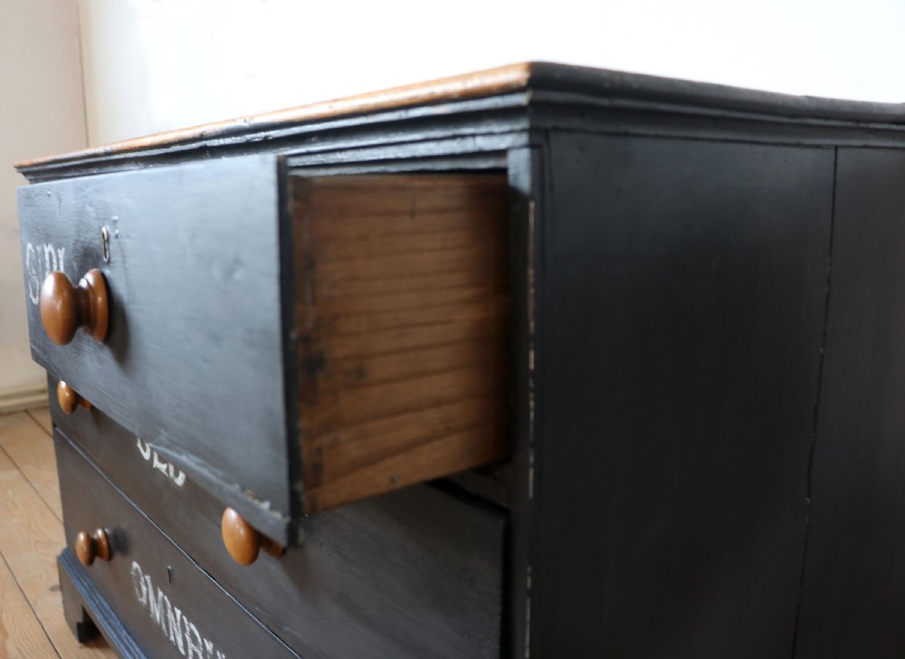 A Victorian black painted pine chest of drawers featuring a natural timber top with hand-painted lettering and turned wooden knobs. View XVI