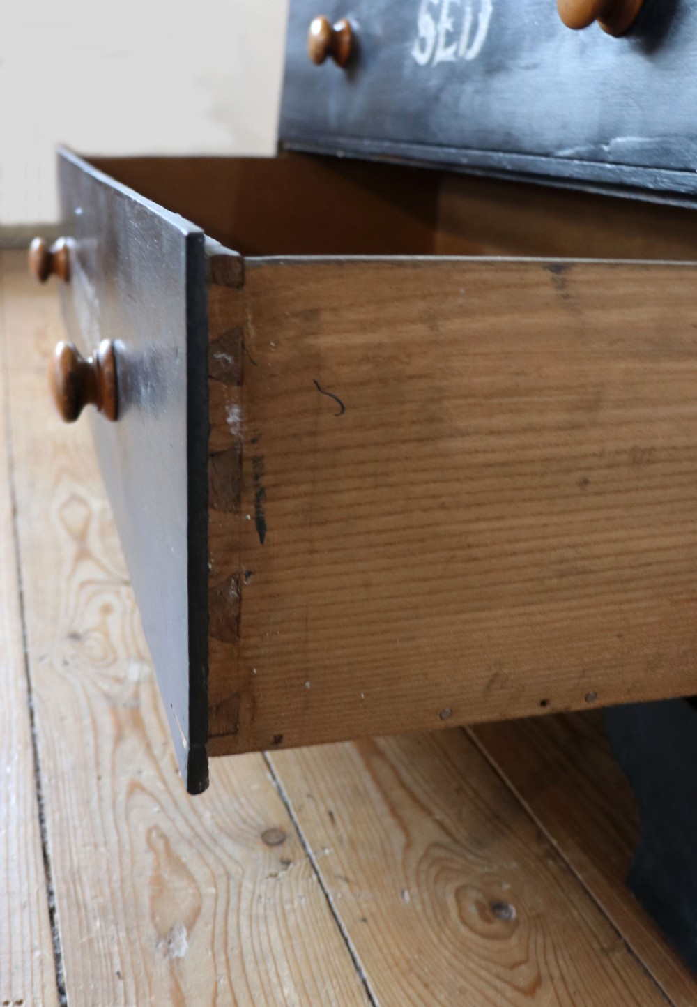 A Victorian black painted pine chest of drawers featuring a natural timber top with hand-painted lettering and turned wooden knobs. View XVII