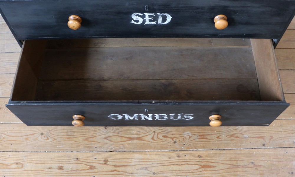A Victorian black painted pine chest of drawers featuring a natural timber top with hand-painted lettering and turned wooden knobs. View XIX