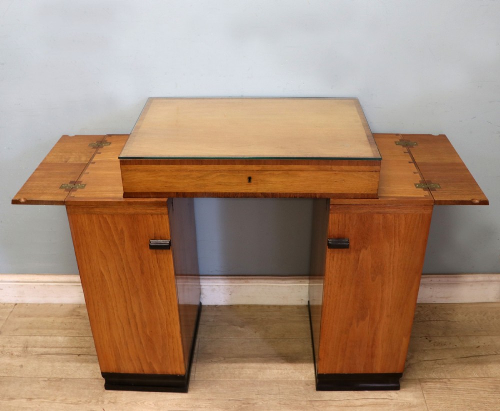 An Art Deco walnut pedestal desk featuring a glass-topped centre writing surface and hinged fold-out side flaps supported by twin cabinet bases.