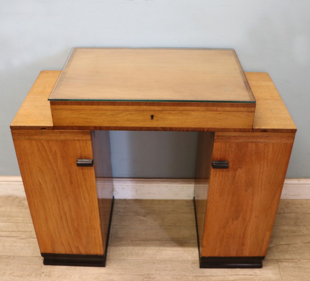 An Art Deco walnut pedestal desk featuring a glass-topped centre writing surface and hinged fold-out side flaps supported by twin cabinet bases. View IV