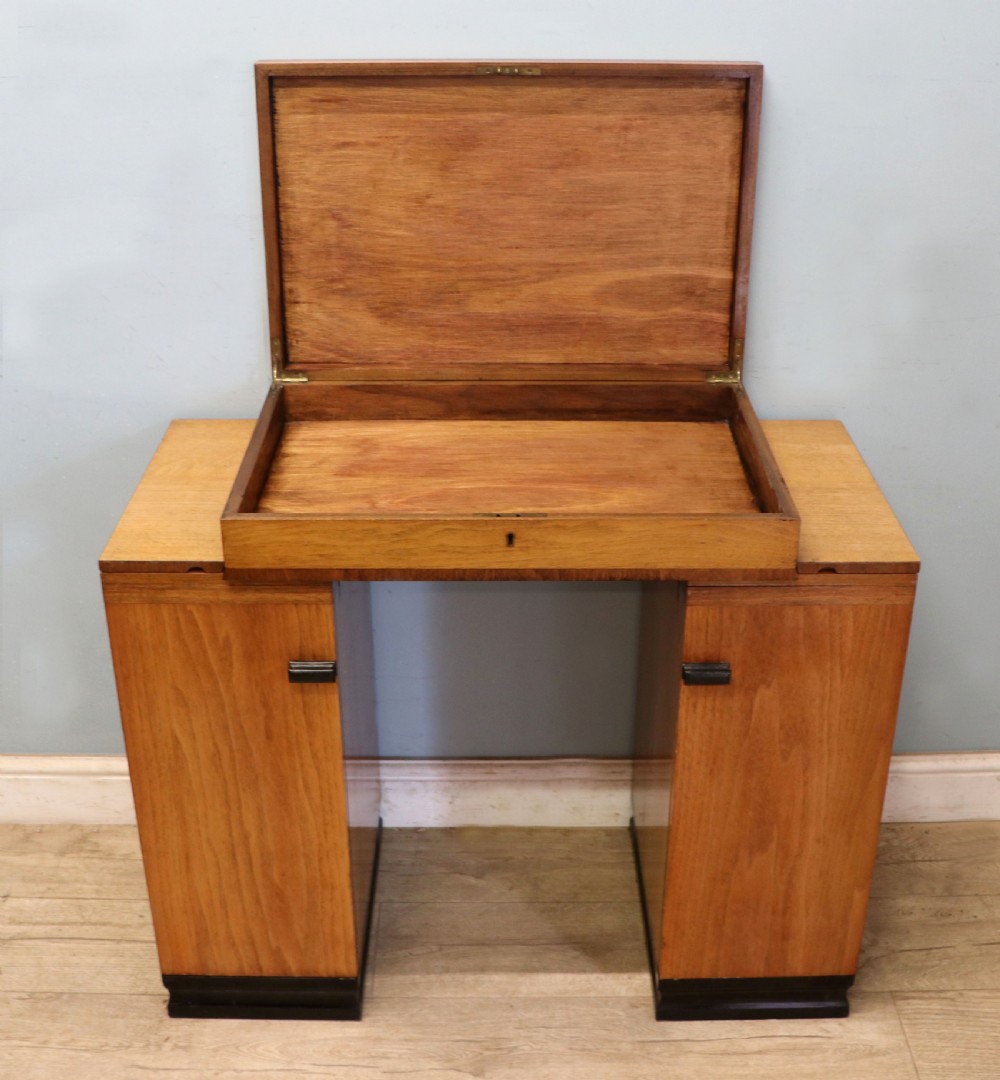 An Art Deco walnut pedestal desk featuring a glass-topped centre writing surface and hinged fold-out side flaps supported by twin cabinet bases. View VI