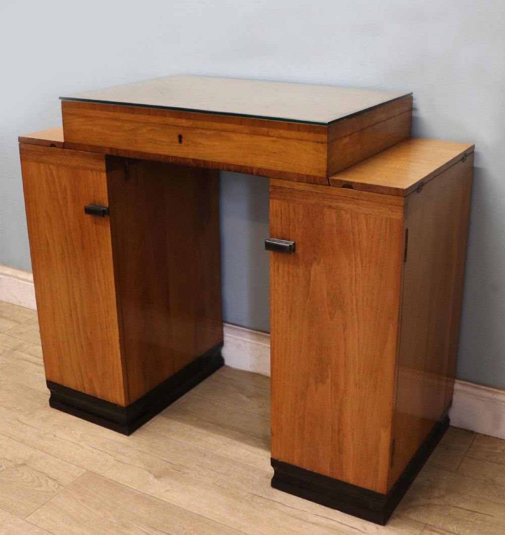 An Art Deco walnut pedestal desk featuring a glass-topped centre writing surface and hinged fold-out side flaps supported by twin cabinet bases. View IX