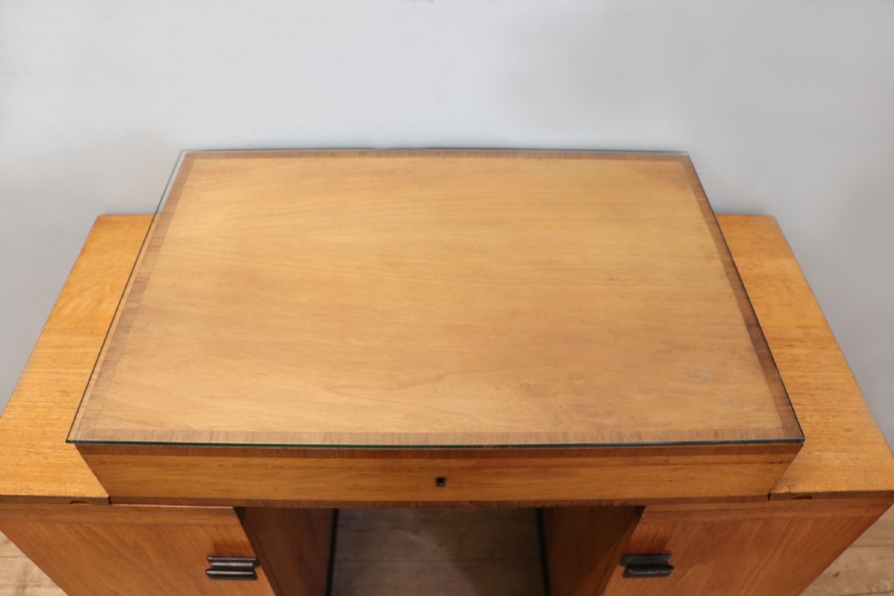An Art Deco walnut pedestal desk featuring a glass-topped centre writing surface and hinged fold-out side flaps supported by twin cabinet bases. View XI