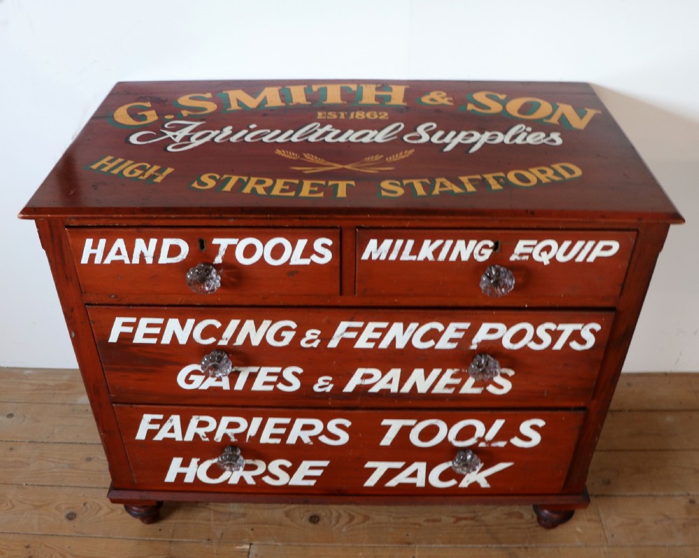 A Victorian red painted pine chest of four drawers featuring white, yellow, and green hand-painted commercial sign-writing and cut glass knobs.