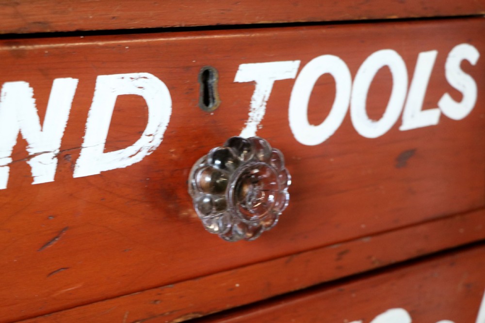 A Victorian red painted pine chest of four drawers featuring white, yellow, and green hand-painted commercial sign-writing and cut glass knobs. View XX