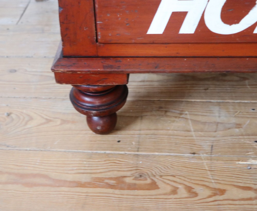 A Victorian red painted pine chest of four drawers featuring white, yellow, and green hand-painted commercial sign-writing and cut glass knobs. View XXV