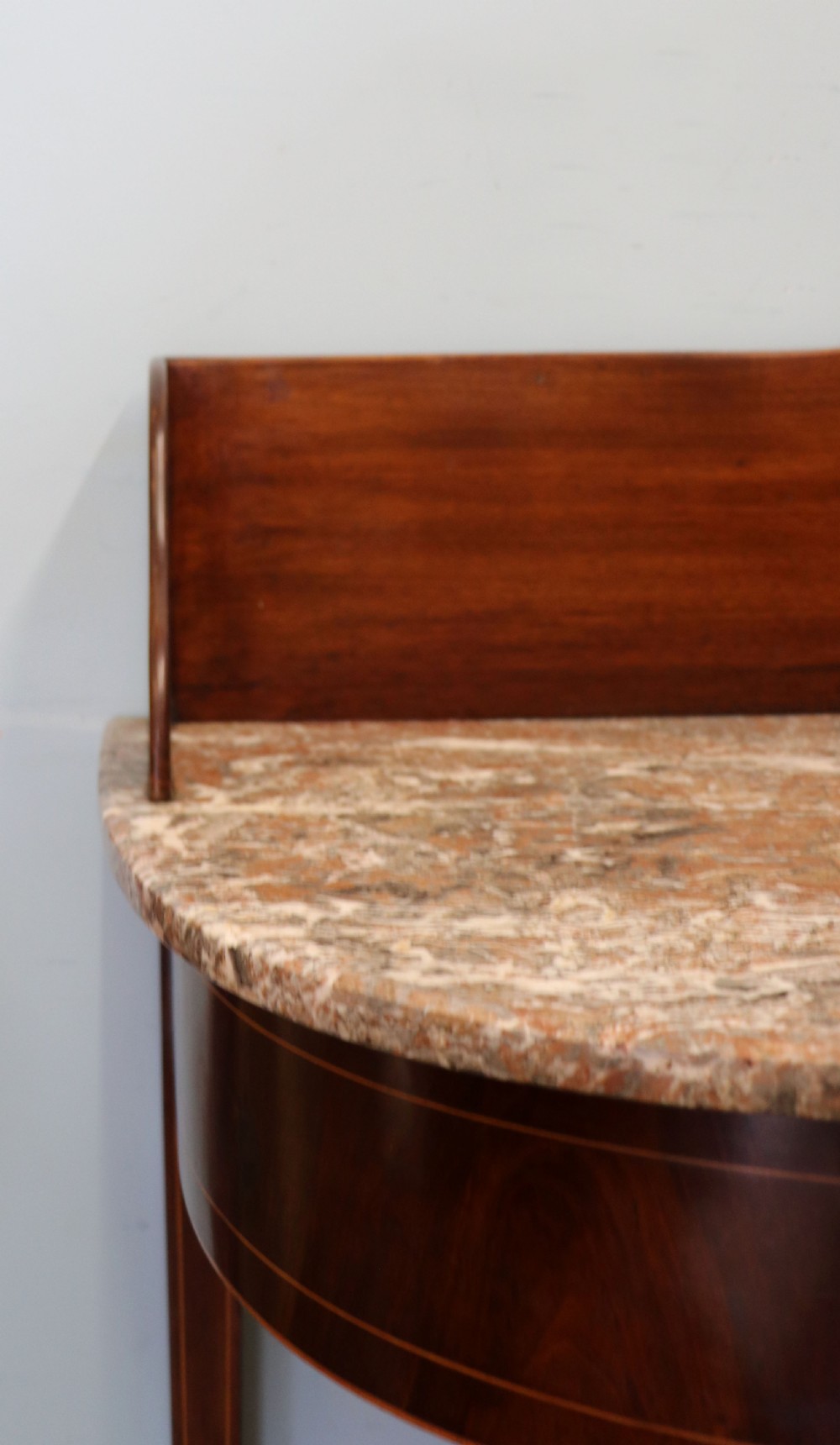 An Edwardian mahogany and satinwood washstand featuring a shaped marble top, wooden splashback, central drawer, and tapered legs on brass castors. View IV
