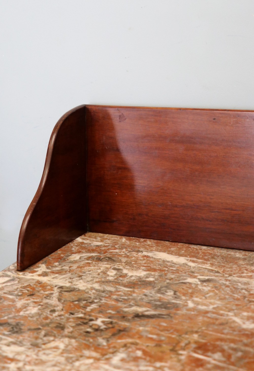 An Edwardian mahogany and satinwood washstand featuring a shaped marble top, wooden splashback, central drawer, and tapered legs on brass castors. View VI