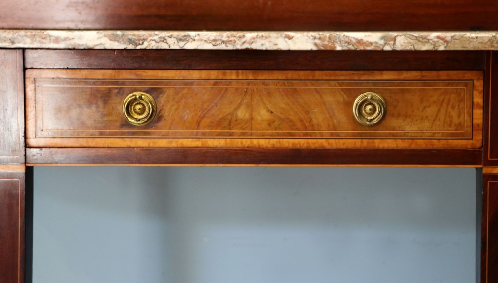 An Edwardian mahogany and satinwood washstand featuring a shaped marble top, wooden splashback, central drawer, and tapered legs on brass castors. View IX