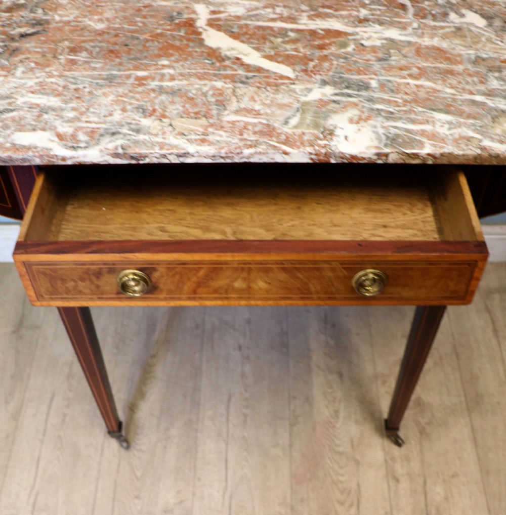 An Edwardian mahogany and satinwood washstand featuring a shaped marble top, wooden splashback, central drawer, and tapered legs on brass castors. View X