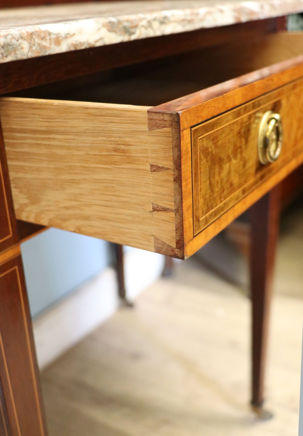 An Edwardian mahogany and satinwood washstand featuring a shaped marble top, wooden splashback, central drawer, and tapered legs on brass castors. View XVI