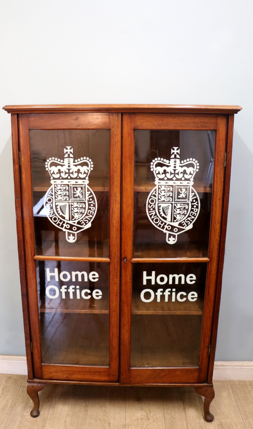 An early twentieth-century mahogany framed bookcase featuring two glazed doors decorated with the Home Office royal coat of arms stencil, supported on cabriole legs.