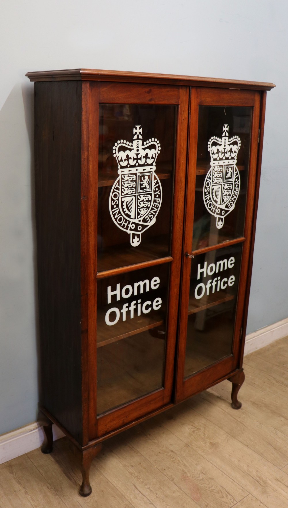 An early twentieth-century mahogany framed bookcase featuring two glazed doors decorated with the Home Office royal coat of arms stencil, supported on cabriole legs. View II