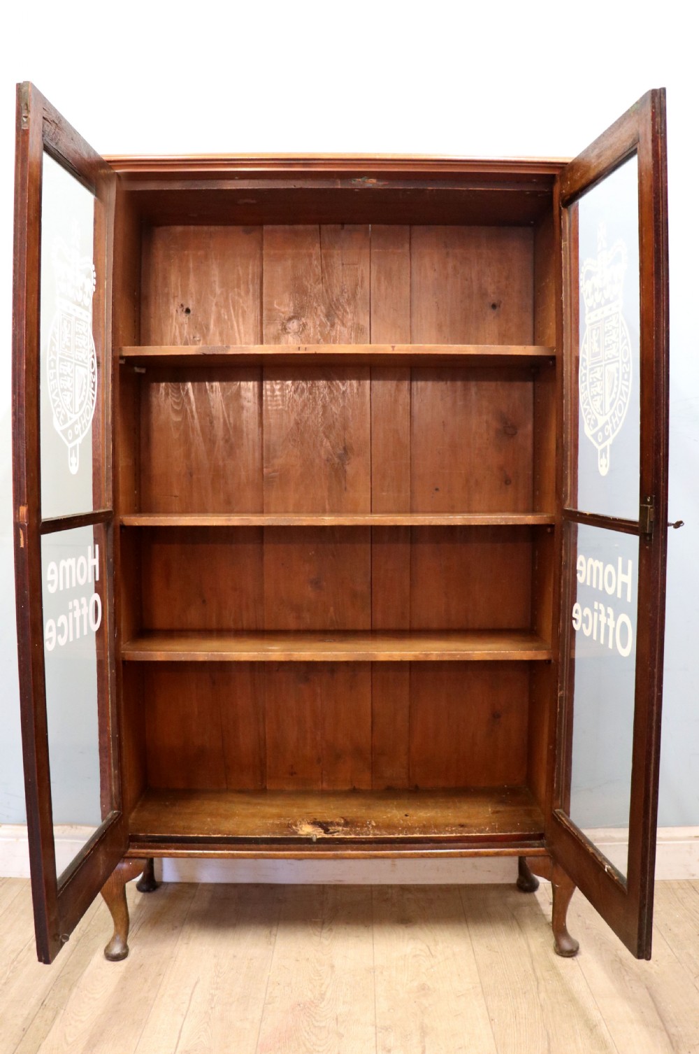 An early twentieth-century mahogany framed bookcase featuring two glazed doors decorated with the Home Office royal coat of arms stencil, supported on cabriole legs. View III