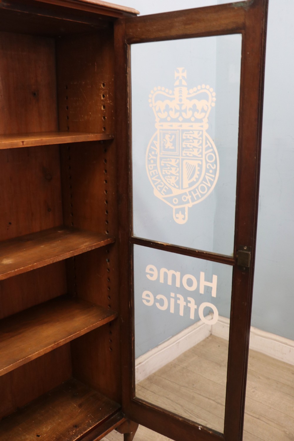 An early twentieth-century mahogany framed bookcase featuring two glazed doors decorated with the Home Office royal coat of arms stencil, supported on cabriole legs. View XV