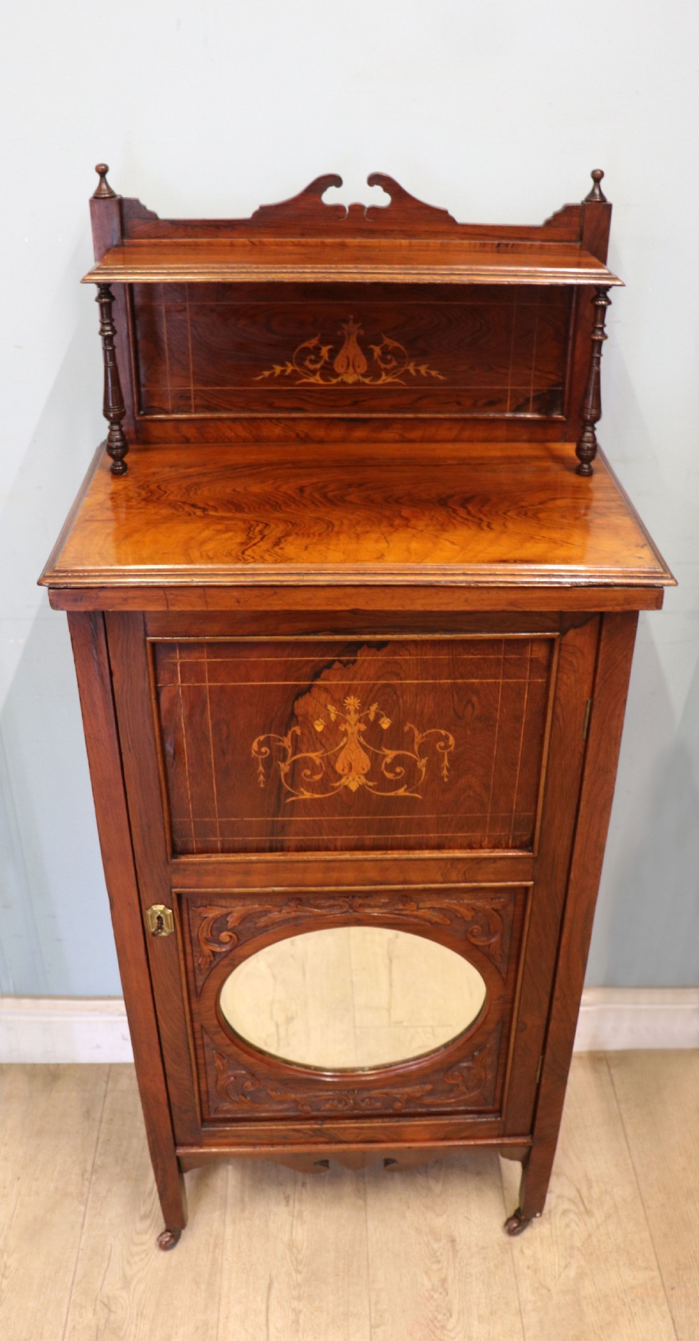 A late nineteenth-century dark hardwood music cabinet featuring floral marquetry inlay on the upper door, an oval mirror panel framed by scroll carving below, and a galleried upper shelf. View II