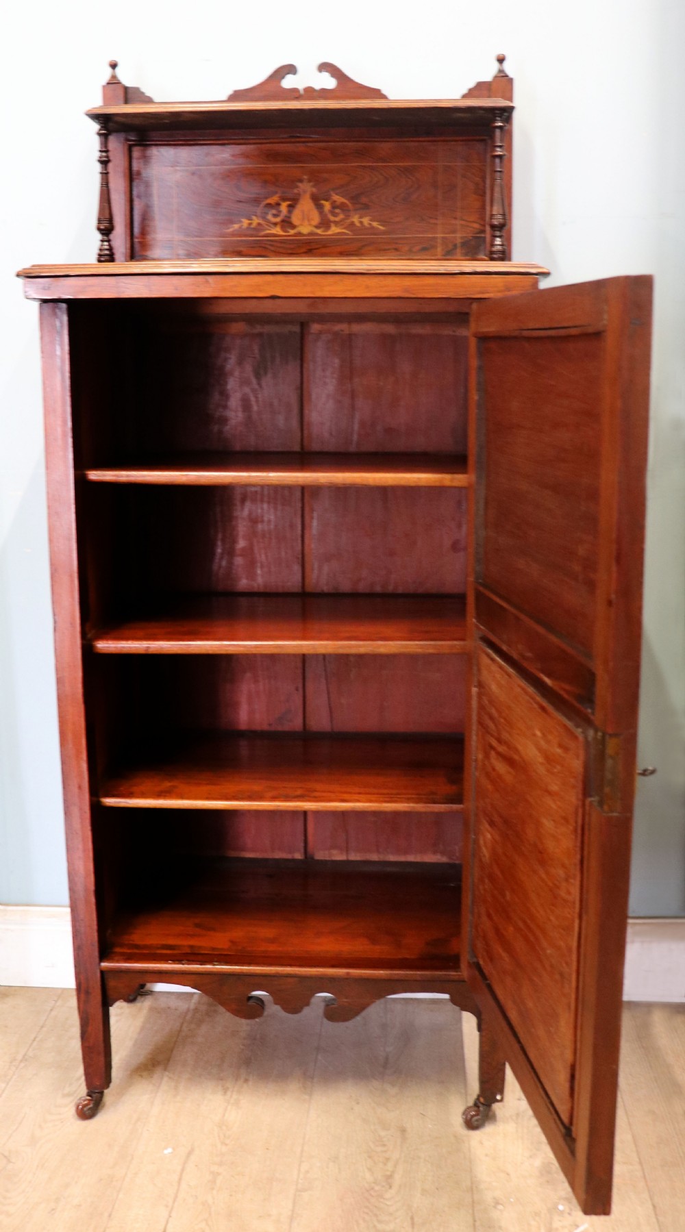 A late nineteenth-century dark hardwood music cabinet featuring floral marquetry inlay on the upper door, an oval mirror panel framed by scroll carving below, and a galleried upper shelf. View III
