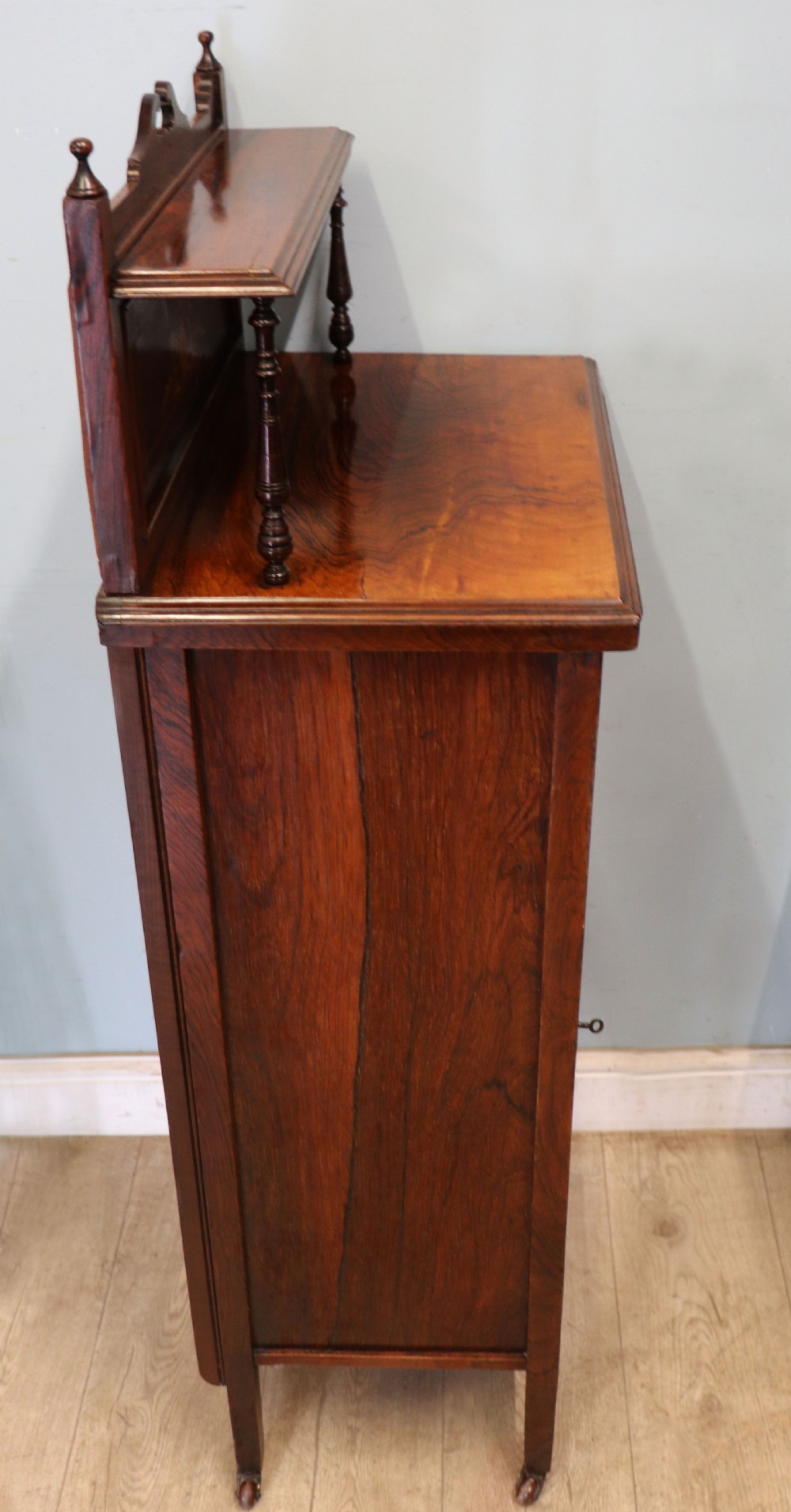 A late nineteenth-century dark hardwood music cabinet featuring floral marquetry inlay on the upper door, an oval mirror panel framed by scroll carving below, and a galleried upper shelf. View V