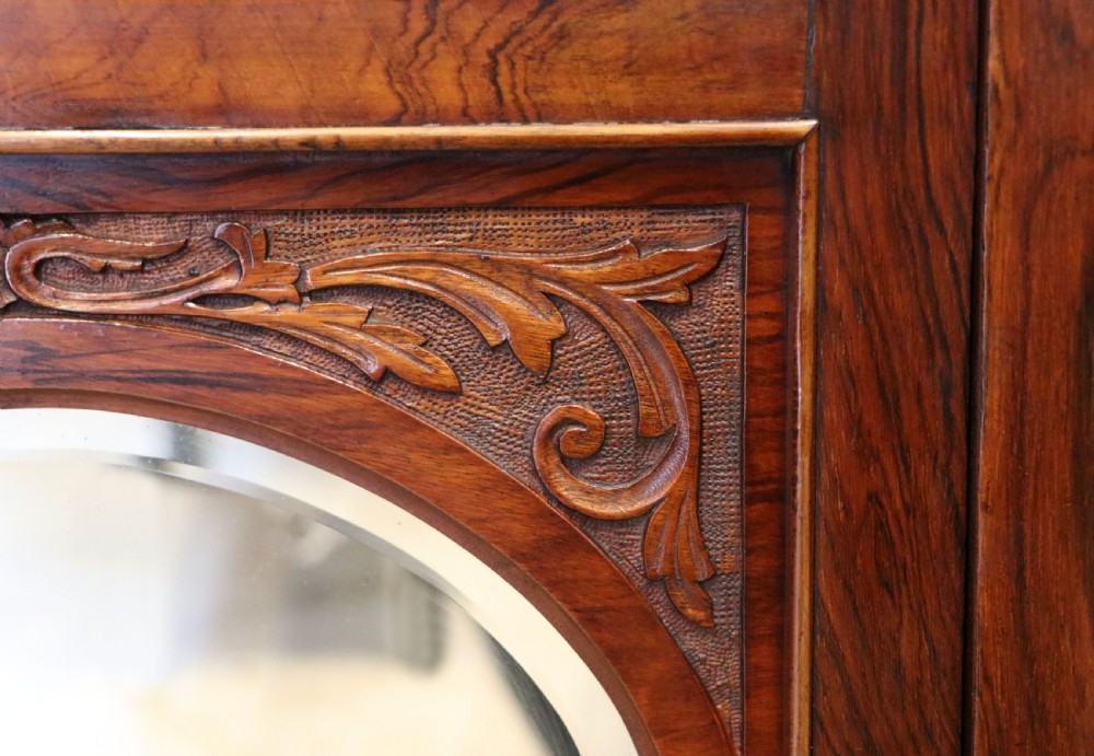 A late nineteenth-century dark hardwood music cabinet featuring floral marquetry inlay on the upper door, an oval mirror panel framed by scroll carving below, and a galleried upper shelf. View XXI