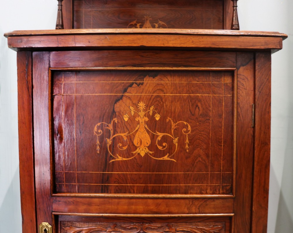 A late nineteenth-century dark hardwood music cabinet featuring floral marquetry inlay on the upper door, an oval mirror panel framed by scroll carving below, and a galleried upper shelf. View XXIV