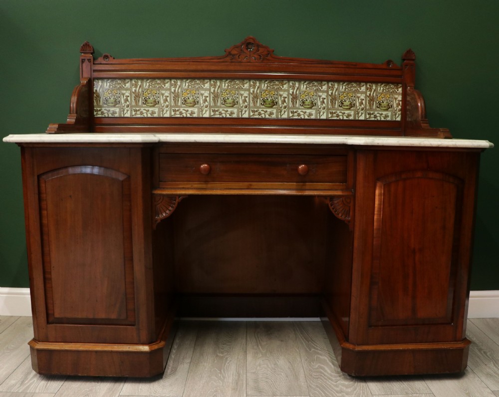 A Victorian Aesthetic Movement mahogany washstand featuring a white marble top, a tiled gallery splashback with floral motifs, two pedestal cupboards, and a central drawer. View II